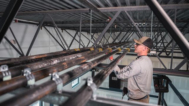 Plumber working on overhead pipe hung below steel roof joists