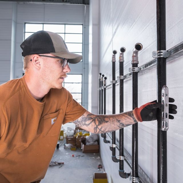 Plumber checking a row of pipe risers strapped to strut channel on a commercial wall