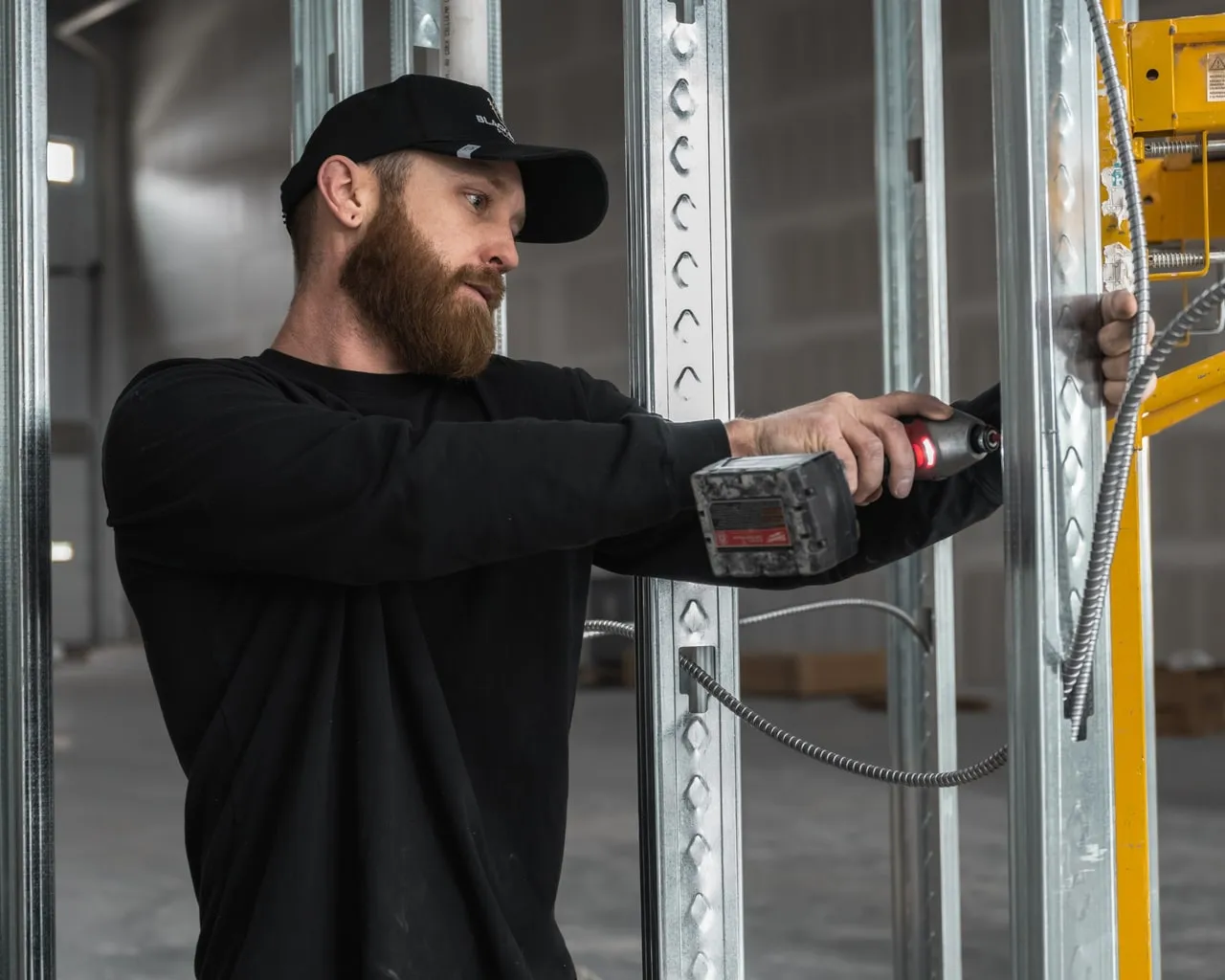Black Forest Plumbing plumber fastening a pipe support to a steel stud with an impact driver