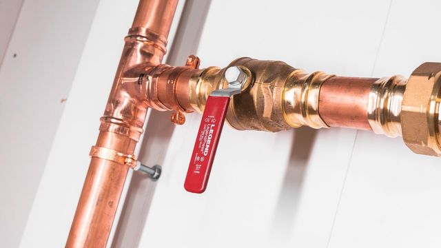 Close-up of a copper press tee and red-handled ball valve