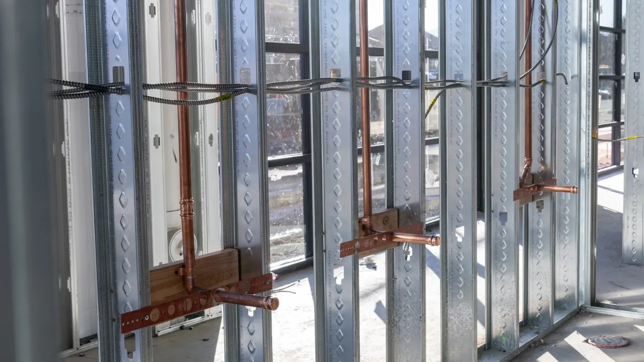 Copper water lines stubbed out through steel studs on a commercial rough-in, each one strapped to a copper bracket
