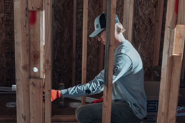 Plumber kneeling inside a wood-framed wall during a new home rough-in