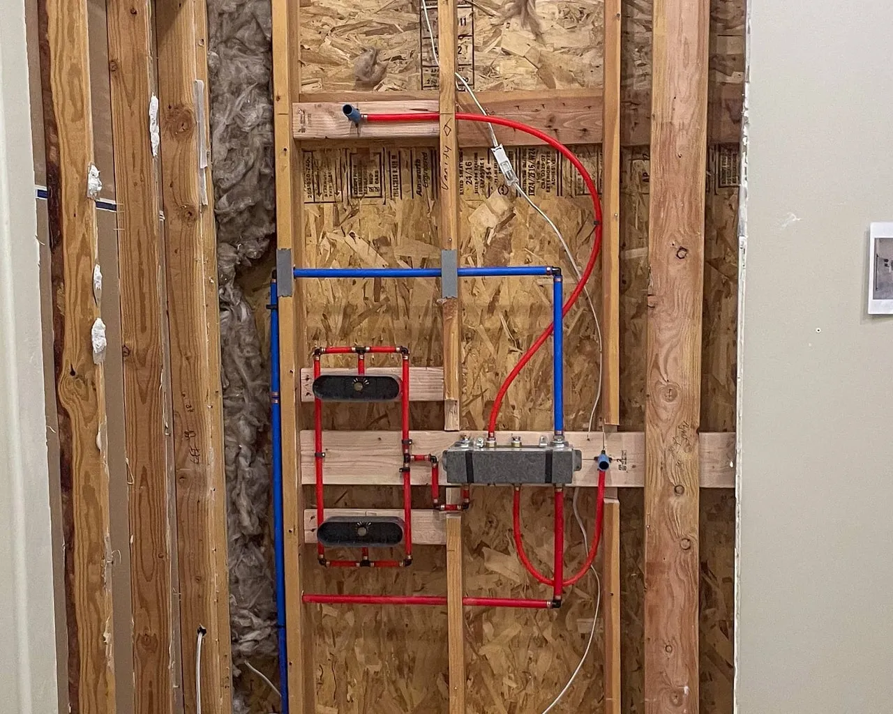 Red and blue PEX water lines roughed in to a shower valve and two wall niches in a wood-framed wall