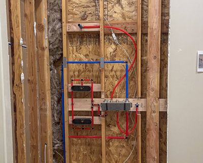 Red and blue PEX water lines roughed in to a shower valve inside a wood-framed wall