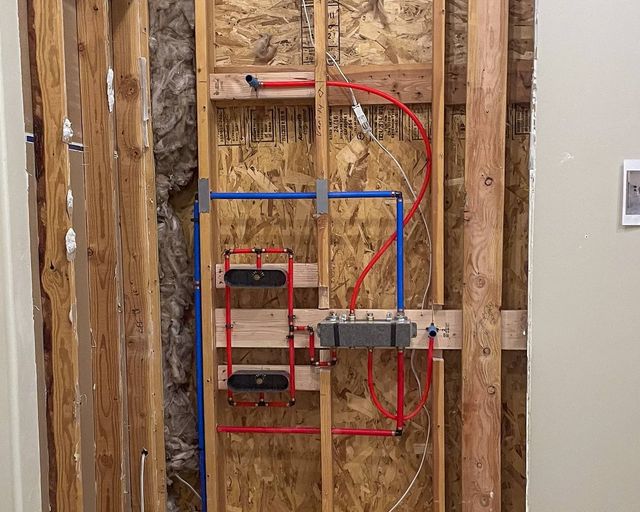 Red and blue PEX lines run to a shower valve and two niches in a wood-framed wall