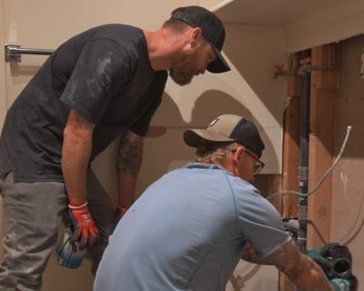 Two Black Forest Plumbing plumbers replacing a drain stack inside an opened wall during a home remodel