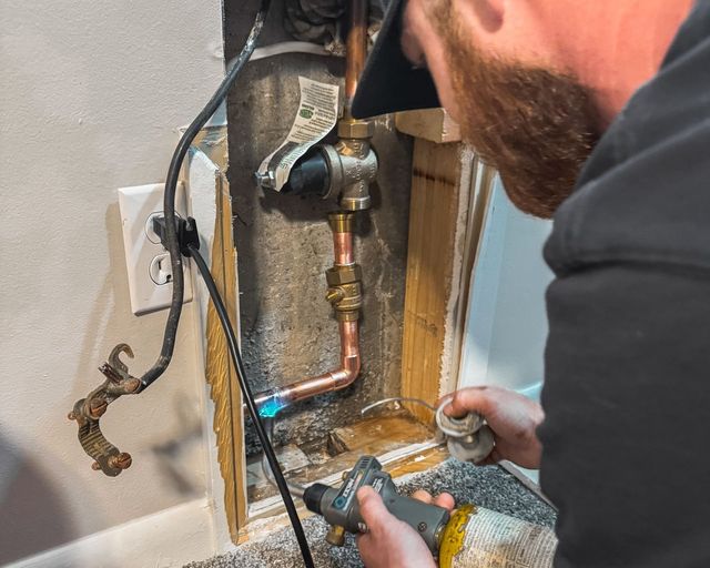 Plumber soldering a copper water line below a pressure regulating valve