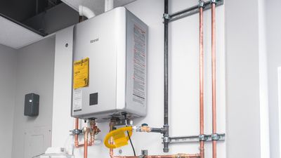 Wall-mounted Rinnai tankless water heater installed by Black Forest Plumbing with copper water lines and a yellow gas connector